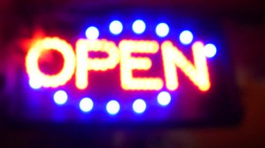 Karanlıkta parlayan açık neon ışığı. Cam pencerenin girişinde canlı retro stil metin var. Renkli elektrikli pankart seçici odaklanma. Ampuller gece parlıyor. Parlak parlak harfler.