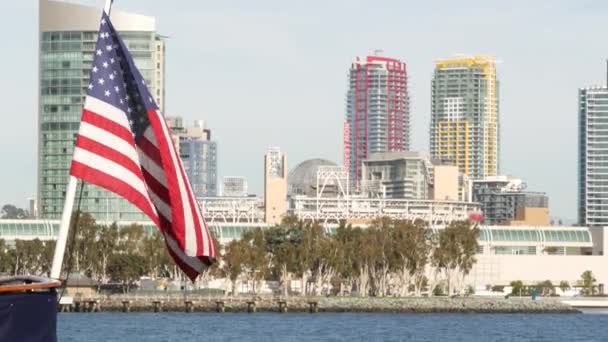 Метрополис, высотные небоскребы в центре города, залив Сан-Диего, Калифорния, США. Здания у береговой линии возле тихоокеанской гавани. Звездно-усыпанное знамя, национальный флаг Старой Славы, размахивающий — стоковое видео