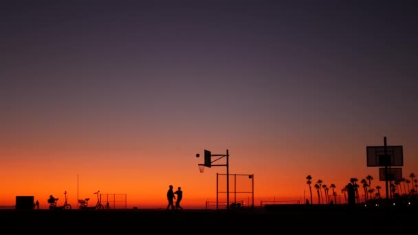 Kalifornia lato zmierzch plaża estetyczne, różowy zachód słońca. Nierozpoznawalne sylwetki, ludzie grają w grę z piłką na boisku do koszykówki. Newport ocean resort w pobliżu Los Angeles CA USA. Purpurowy gradient nieba — Wideo stockowe