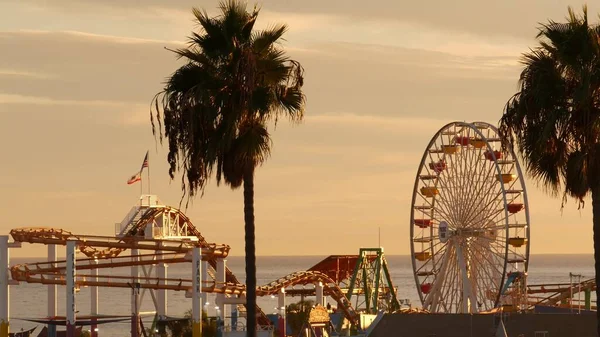 Classic ferris wheel, amusement park on pier in Santa Monica pacific ocean beach resort. Summertime California aesthetic, iconic view, symbol of Los Angeles, CA USA. Sunset golden sky and attractions.