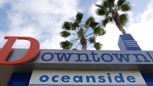 Oceanside nameboard sign and palm trees. Oside is the popular american tourist resort, pacific ocean west coast, San Diego County, California USA. Name of city of vacations and tourism on coastline.