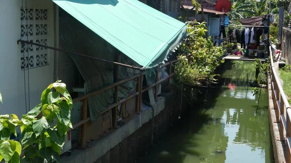 Oriental slum near channel. Shabby houses of typical oriental slum located near small canal on street of Bangkok on sunny day. Poor traditional living near water in houses on stilts — Stock Image Oriental Slum Channel Shabby Houses Typical Oriental Slum Located Small Stock Picture