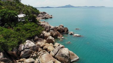 Tropikal adada küçük evler. Güneşli Tayland 'da güneşli bir günde, Koh Samui adasının kıyısındaki küçük, rahat bungalovlar. Volkanik kayalar ve uçurumlar insansız hava aracı görüntüsü