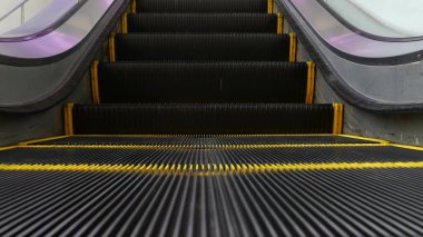 Modern yürüyen merdivenlerin alçak açılı perspektifli görüntüsü. Otomatik asansör mekanizması. Merdivenlerdeki sarı çizgi mor ışıkla aydınlatılmış. Gelecekçi boş makine merdiveni dümdüz ilerliyor.