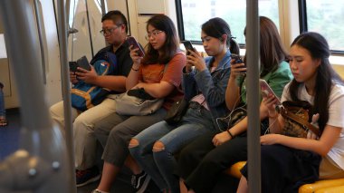 BANGKOK, THAILAND - 13 HAZİRAN, 2019: akıllı telefonları kullanan Asyalı yolcular. Taylandlılar BT 'nin arabasıyla internette sörf yapıyor. Toplu taşıma. Metroda sosyal medya ve telefondan bağımlılık