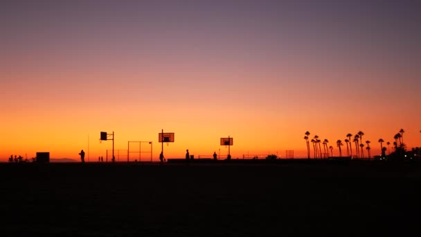 Californie été crépuscule plage esthétique, coucher de soleil rose. Silhouettes méconnaissables, les gens jouent avec la balle sur le terrain de basket-ball. Station balnéaire de Newport près de Los Angeles CA USA. Gradient de ciel violet — Video