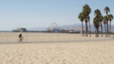 Kaliforniya plaj estetiği, insanlar bisiklet yolunda bisiklet sürüyor. Bulanık, odaklanmış arka plan. Santa Monica Amerikan Pasifik Okyanusu Tatil Köyü, Los Angeles CA ABD 'deki iskele ve palmiyelerdeki eğlence parkı.