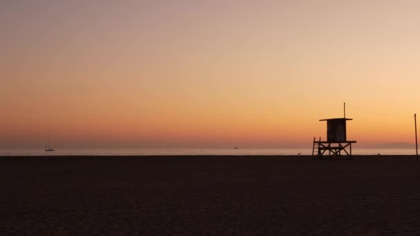 Kesämatkakonsepti. Tumma siluetti, ikoninen retro puinen hengenpelastaja vartiotorni auringonlaskua vastaan oranssi taivas. Kontrasti vartiotorni ääriviivat, Kaliforniassa Tyynenmeren rannalla hämärä esteettinen, CA USA — kuvapankkivideo