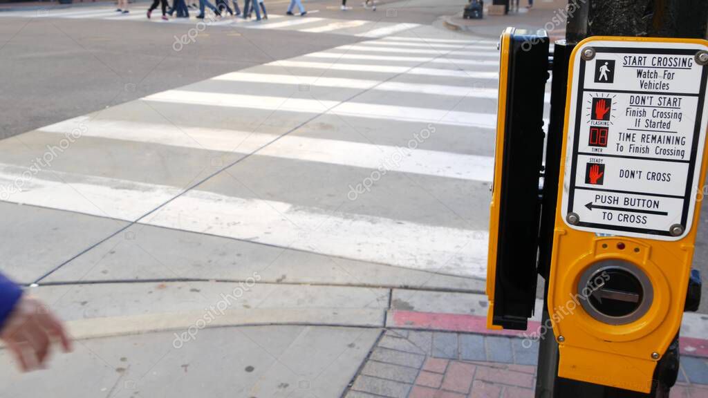 Traffic light button on pedestrian crosswalk, people have to push and wait. Traffic rules and regulations for public safety in USA. Zebra street crossing on road intesection in San Diego, California.