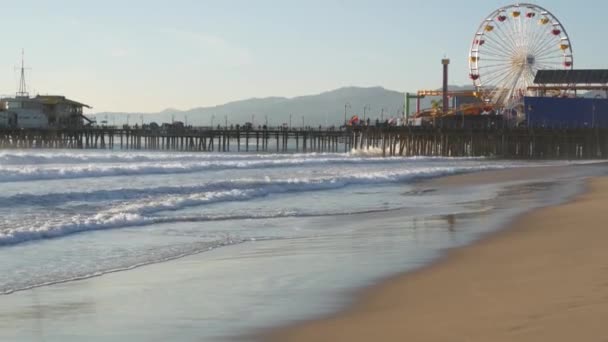 Ωκεάνια κύματα και αμμώδης παραλία της Καλιφόρνια, κλασικό τροχό λούνα παρκ στην προβλήτα στη Σάντα Μόνικα Πασίφικ Ωκεανό θέρετρο. Καλοκαίρι εικονική θέα, σύμβολο του Λος Άντζελες, CA ΗΠΑ. Ταξιδιωτική έννοια — Αρχείο Βίντεο