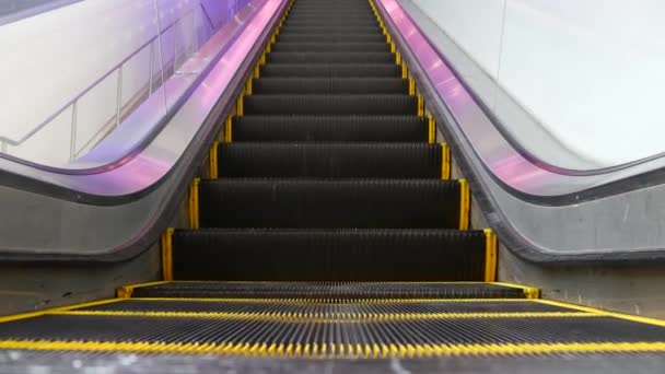 Vista en bucle de ángulo bajo de escaleras mecánicas modernas. Mecanismo de ascensor automatizado. Línea amarilla en escalera iluminada con luz púrpura. Escalera de maquinaria vacía futurista moviéndose recta — Vídeo de stock