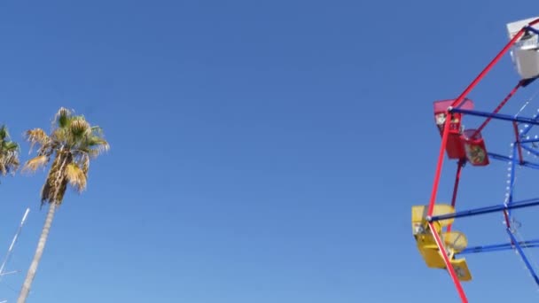 Classique été vif, amusant et symbole d'enfance, feuilles de palmier tropical vert. Iconique attraction de roue rétro ferris coloré. Newport, Californie Pacifique station balnéaire près de Los Angeles USA — Video