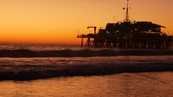 Kalifornská letní pláž estetická, zlatý západ slunce. Živé nebe nad oceánskými vlnami. Santa Monica populární resort, Los Angeles CA USA. Slavné molo proti atmosférickému náladovému západu slunce v LA — Stock video