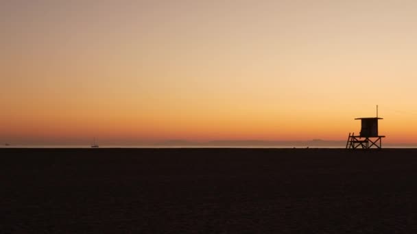 Concetto di viaggio estivo. Silhouette scura, iconica torre di guardia in legno retrò bagnino contro il tramonto cielo arancione. Profilo della torre di avvistamento a contrasto, California Pacific Ocean Beach Twilight estetica, CA USA — Video Stock