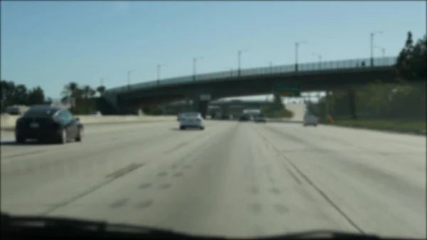 Driving on intercity freeway in Los Angeles, California USA. Defocused view from car thru glass windshield on busy interstate highway. Blurred suburb multiple lane driveway. Camera inside auto in LA.