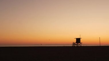 Yaz seyahati konsepti. Karanlık siluet, ikonik retro ahşap cankurtaran kulesi günbatımı turuncu gökyüzüne karşı. Karşıt Gözetleme Kulesi Hattı, Kaliforniya Pasifik Okyanusu Sahili alacakaranlık estetiği, CA USA