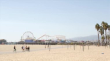 Kaliforniya plaj estetiği, insanlar bisiklet yolunda bisiklet sürüyor. Bulanık, odaklanmış arka plan. Santa Monica Amerikan Pasifik Okyanusu Tatil Köyü, Los Angeles CA ABD 'deki iskele ve palmiyelerdeki eğlence parkı.