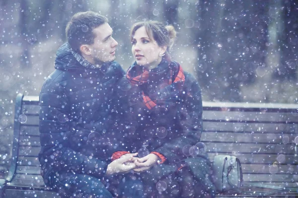 young man and woman sitting on bench together in winter park, romantic happy couple