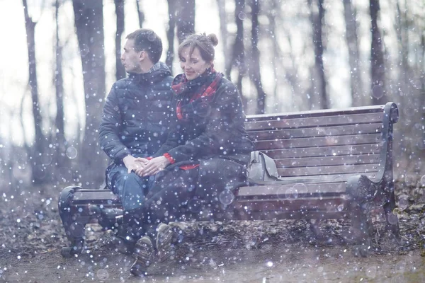 young man and woman sitting on bench together in winter park, romantic happy couple