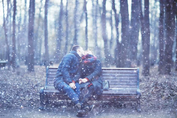 young man and woman sitting on bench together in winter park, romantic happy couple