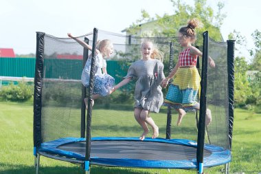 three little girls sisters jumping on trampoline outdoors in summer clipart