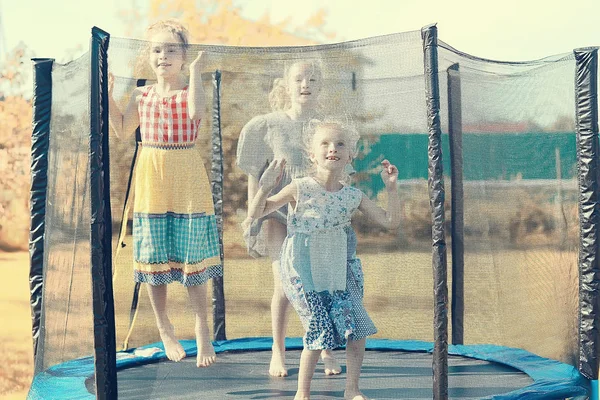 三个小女孩姐妹在夏天在户外的蹦床上跳来跳去 — 图库照片