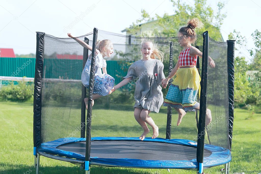three little girls sisters jumping on trampoline outdoors in summer