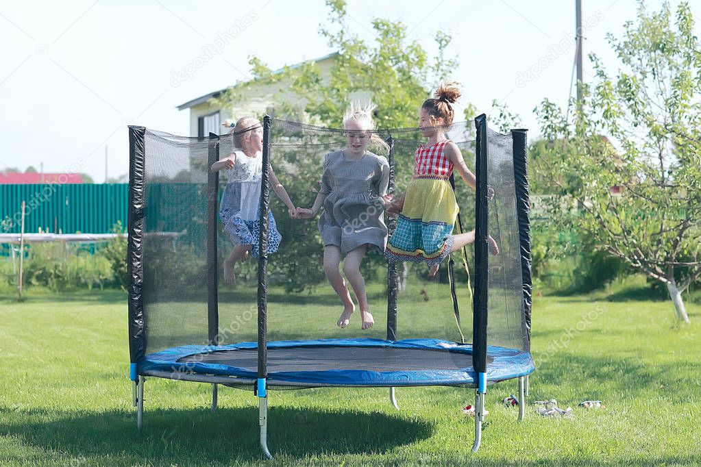 three little girls sisters jumping on trampoline outdoors in summer