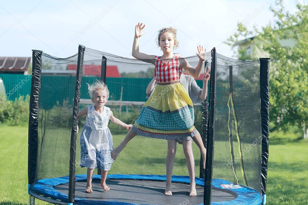 three little girls sisters jumping on trampoline outdoors in summer