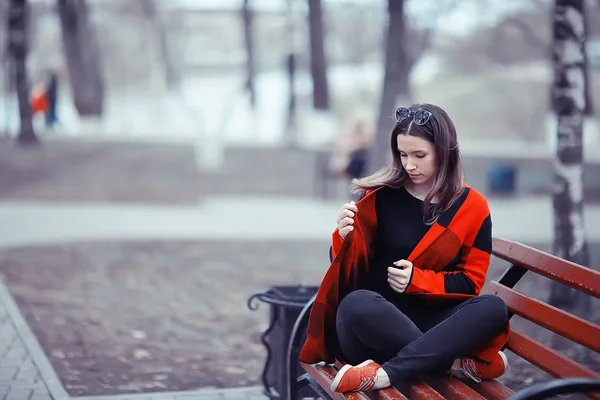 秋の公園でベンチに座っている格子縞のコートで若い美しい女性 — ストック写真