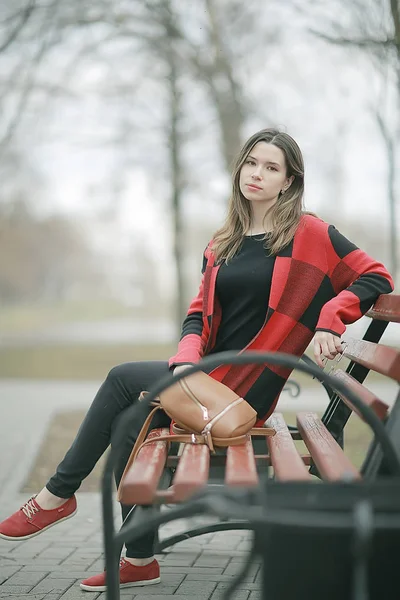 在秋季公园长凳上坐在格子大衣的年轻美丽的妇女 — 图库照片