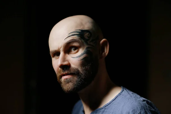 portrait of brutal bearded man with tattoo on face