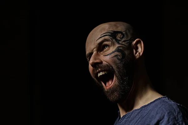 portrait of brutal bearded man with tattoo on face