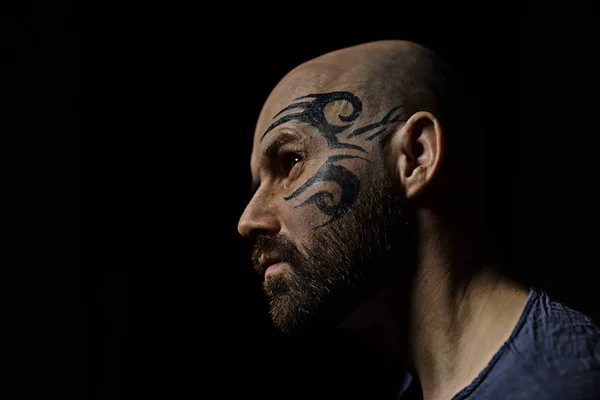 portrait of brutal bearded man with tattoo on face