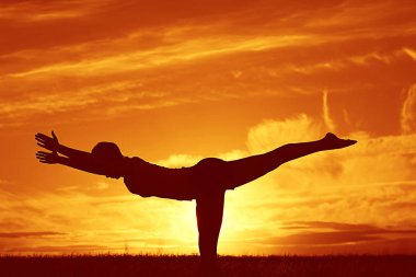 Gün batımında yoga yaz Lawn yaparken genç kadın silüeti 