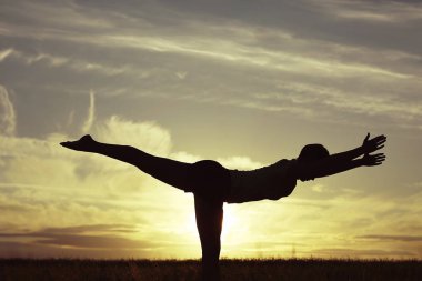 Gün batımında yoga yaz Lawn yaparken genç kadın silüeti 