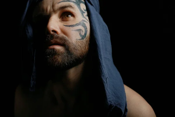 portrait of brutal bearded man with tattoo on face