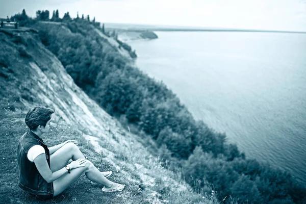 川の土手に座っている孤独な若い美しい若い女性の肖像画 — ストック写真