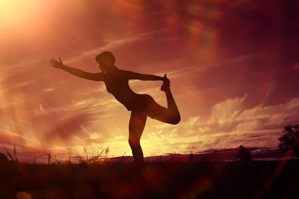 Silhouette of young woman doing yoga at summer lawn at sunset