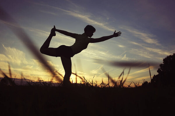 Silhouette of young woman doing yoga at summer lawn at sunset 