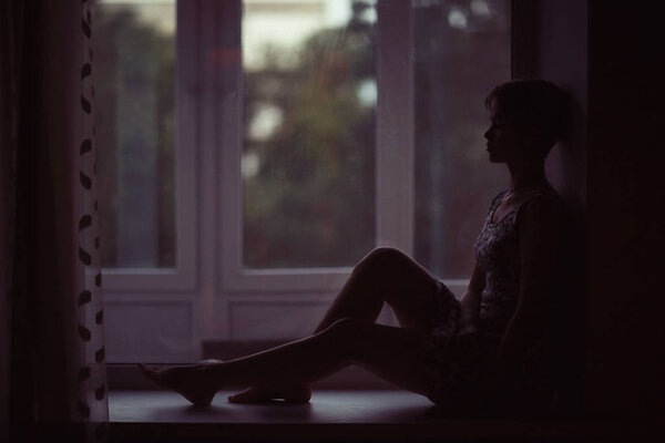 portrait of dreamy young woman sitting on a windowsill at home