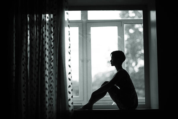 portrait of dreamy young woman sitting on a windowsill at home