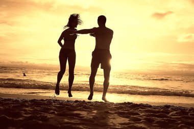 mutlu aşıklar kumlu plajda, gün batımı görünümü siluetleri. Yeni evliler ve denizde resort balayı. 