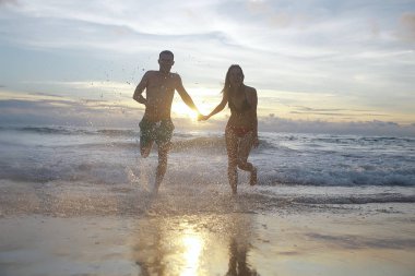 mutlu aşıklar kumlu plajda, gün batımı görünümü siluetleri. Yeni evliler ve denizde resort balayı. 