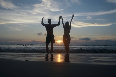 mutlu aşıklar kumlu plajda, gün batımı görünümü siluetleri. Yeni evliler ve denizde resort balayı. 