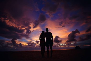 mutlu aşıklar kumlu plajda, gün batımı görünümü siluetleri. Yeni evliler ve denizde resort balayı. 