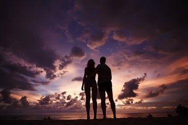 mutlu aşıklar kumlu plajda, gün batımı görünümü siluetleri. Yeni evliler ve denizde resort balayı. 