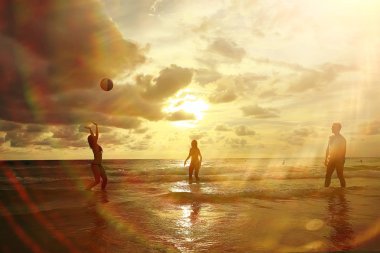 Sahilde günbatımı, sağlıklı dinlenme, spor etkinliği, yaz tatili ile top oynarken sporcuların siluetleri
