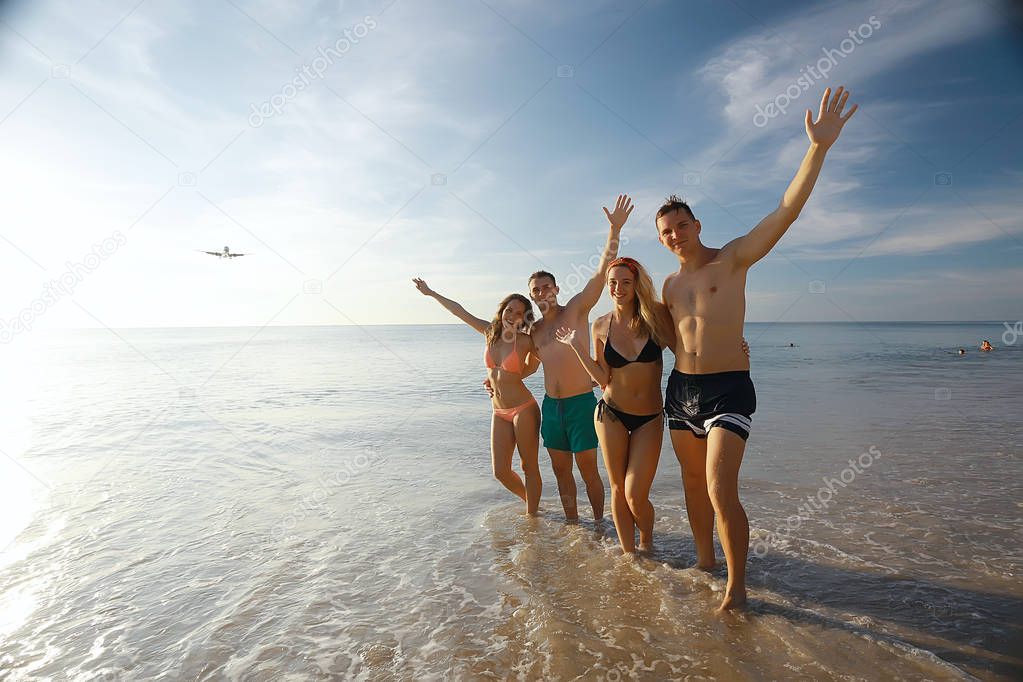 four friends running on beach,  summer vacation and happiness concept. Young men and women having fun at sea shore