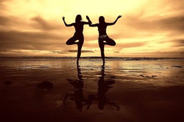 meditasyon ve yoga sahilde. Deniz kıyısında yoga yaparken iki genç kadın